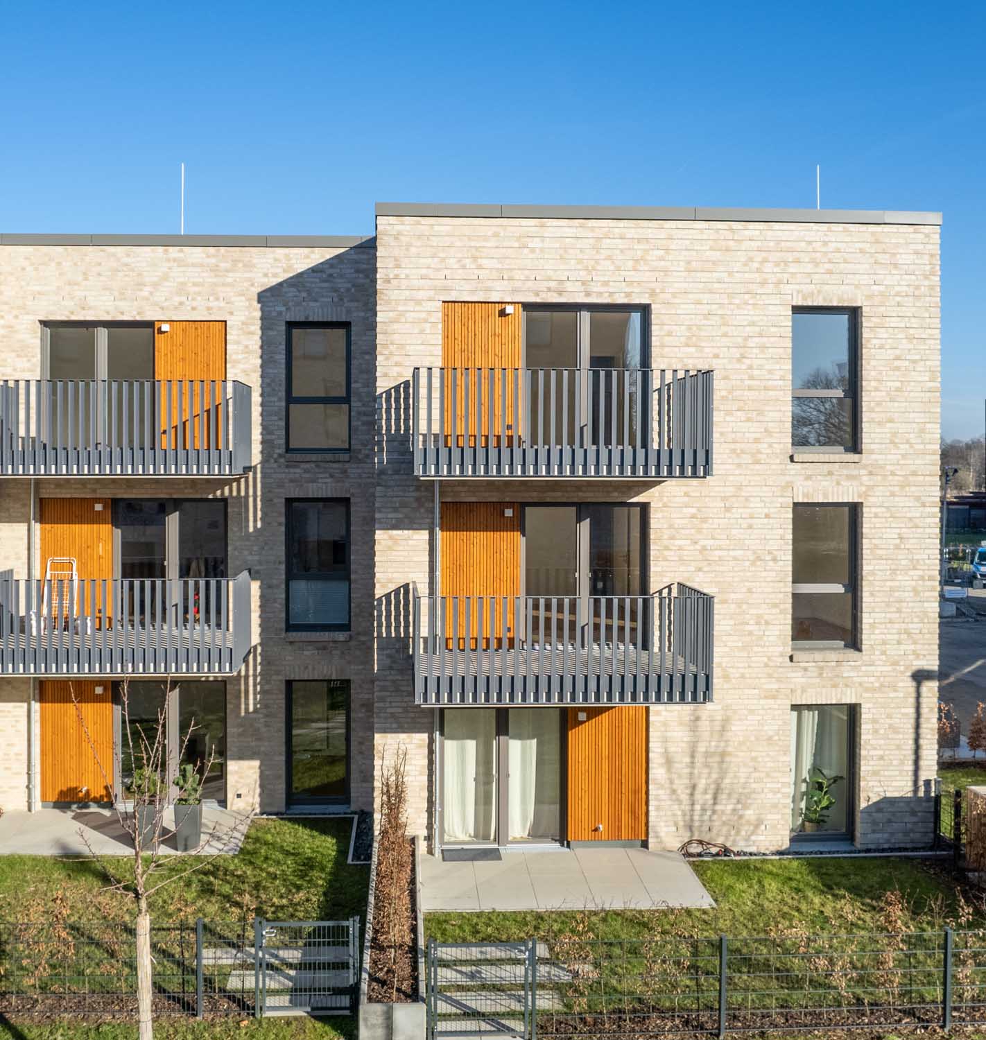Fertiges Wohnhaus mit hellen Klinkern, Balkonen und orangefarbenen Türen