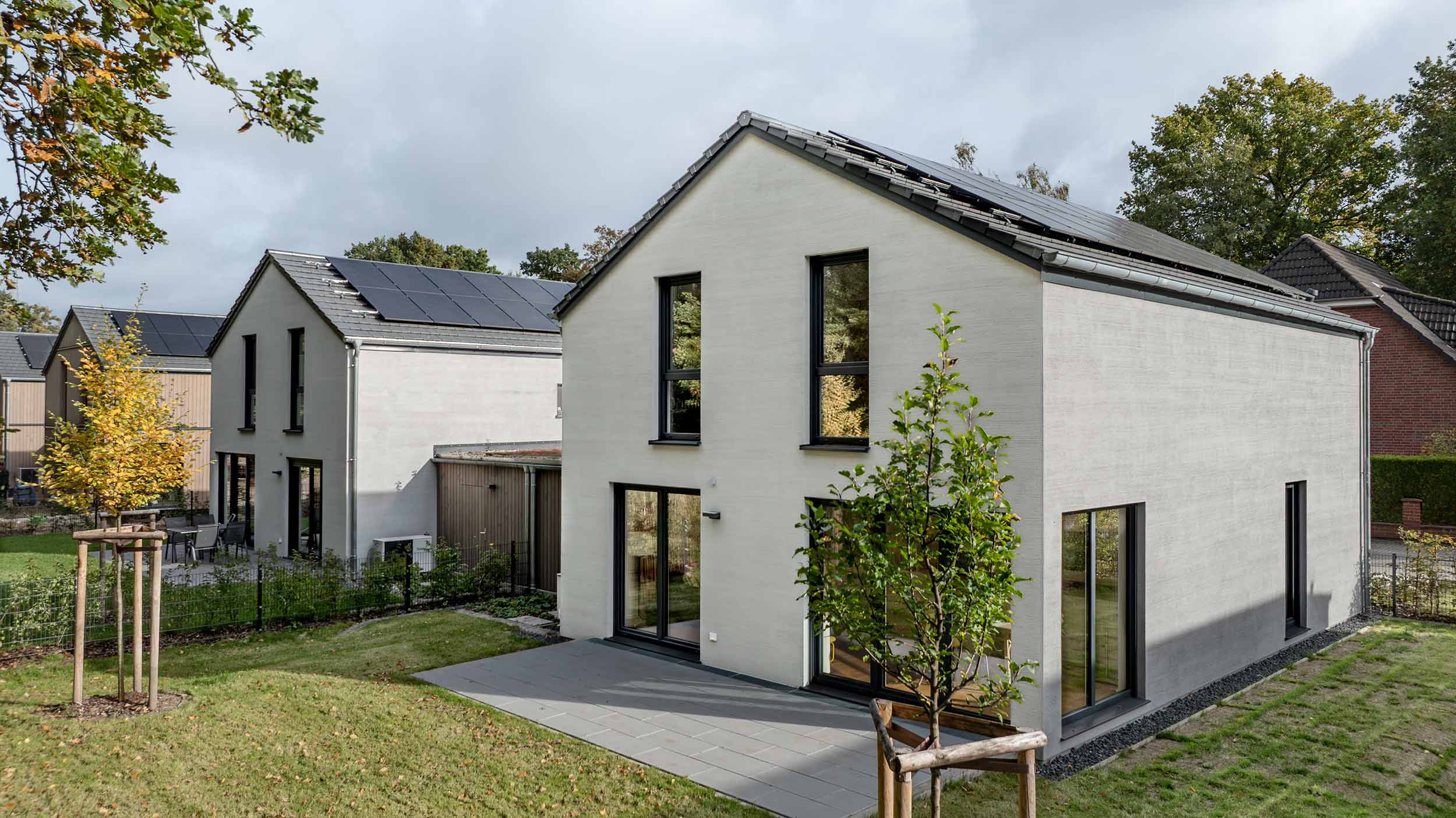 Einfamilienhaus mit Satteldach und Photovoltaik, davor junger Baum und Garten