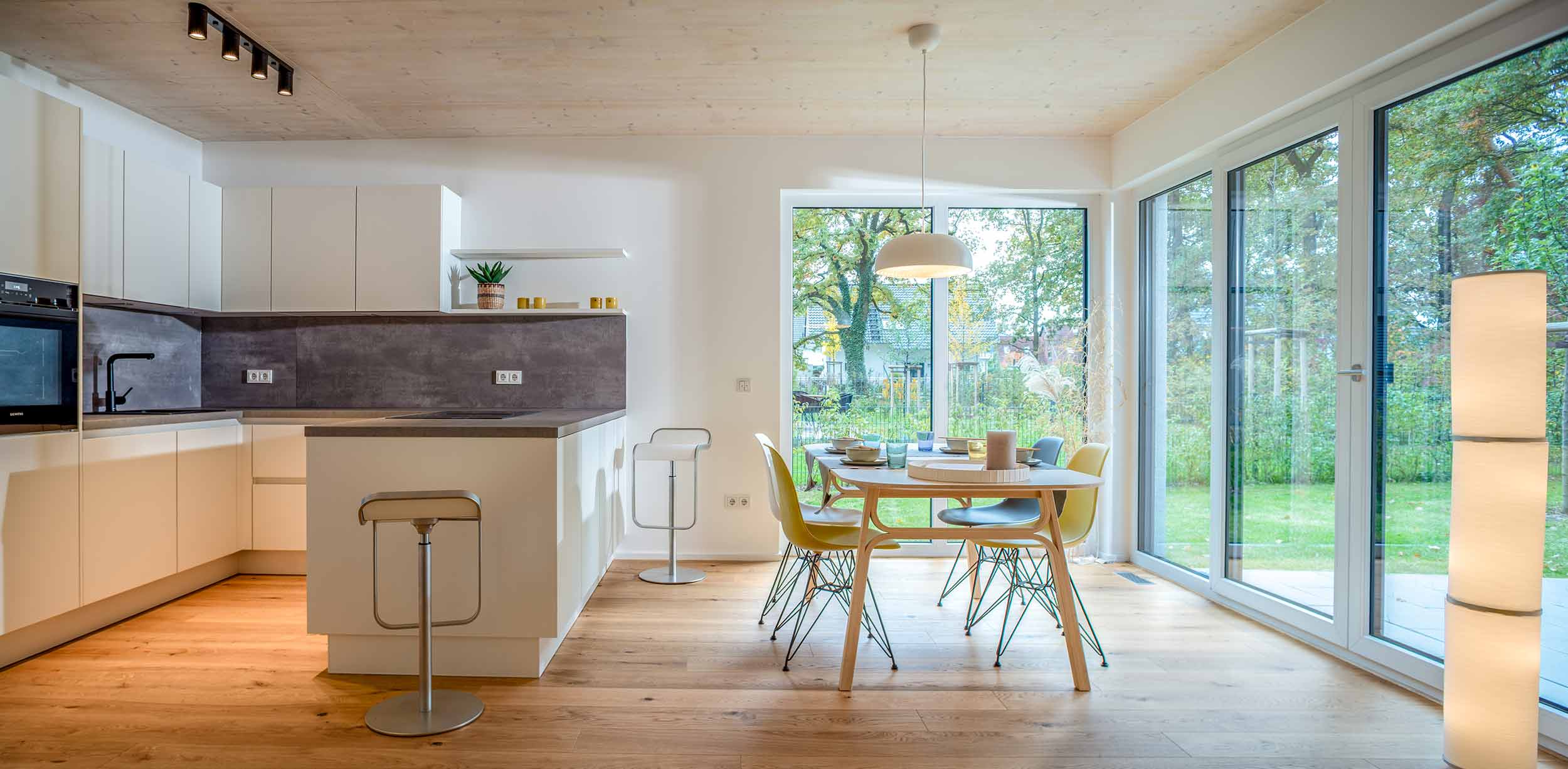 Offene Wohnküche mit Holzboden, Esstisch und bodentiefen Fenstern zum Garten