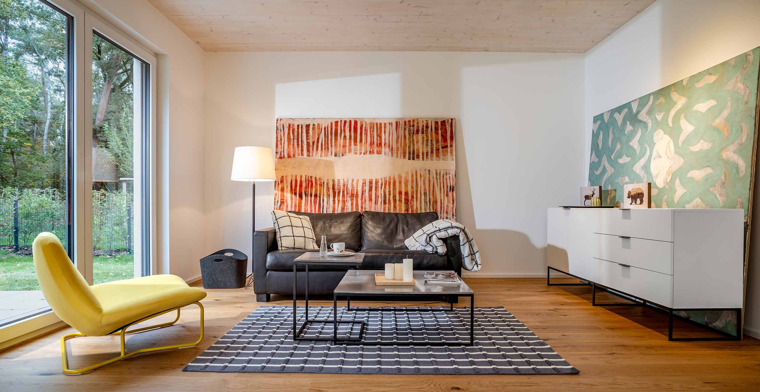 Eingerichtetes Wohnzimmer mit gelbem Sessel, Sofa und großen Fenstern